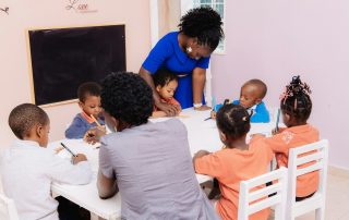 Maestra guiando a niños que dibujan en una mesa del salón